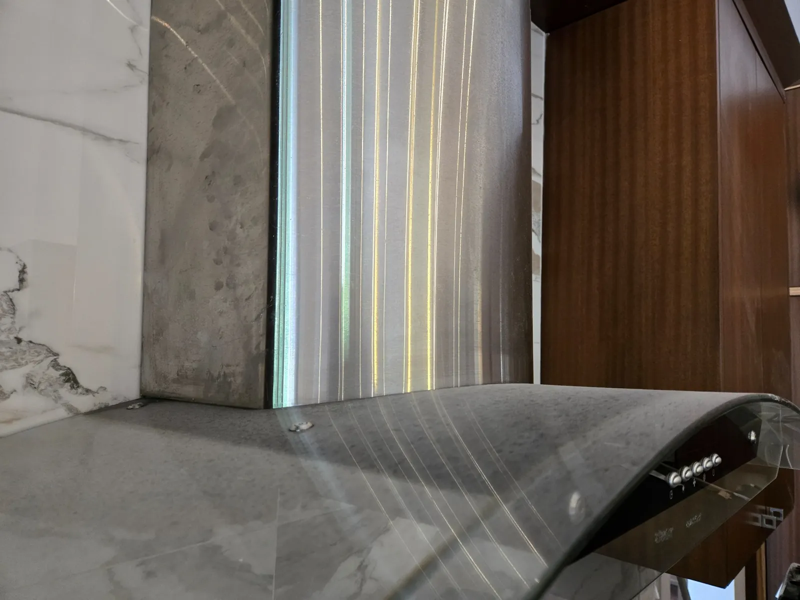 A layer of fine grey dust on top of a stainless-steel range hood with a curved glass canopy, before cleaning